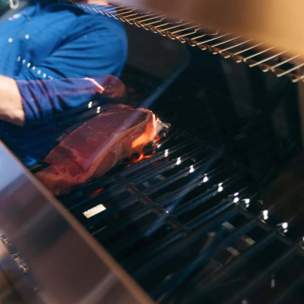 Person grilling a piece of meat on a Monument Grills Denali 605