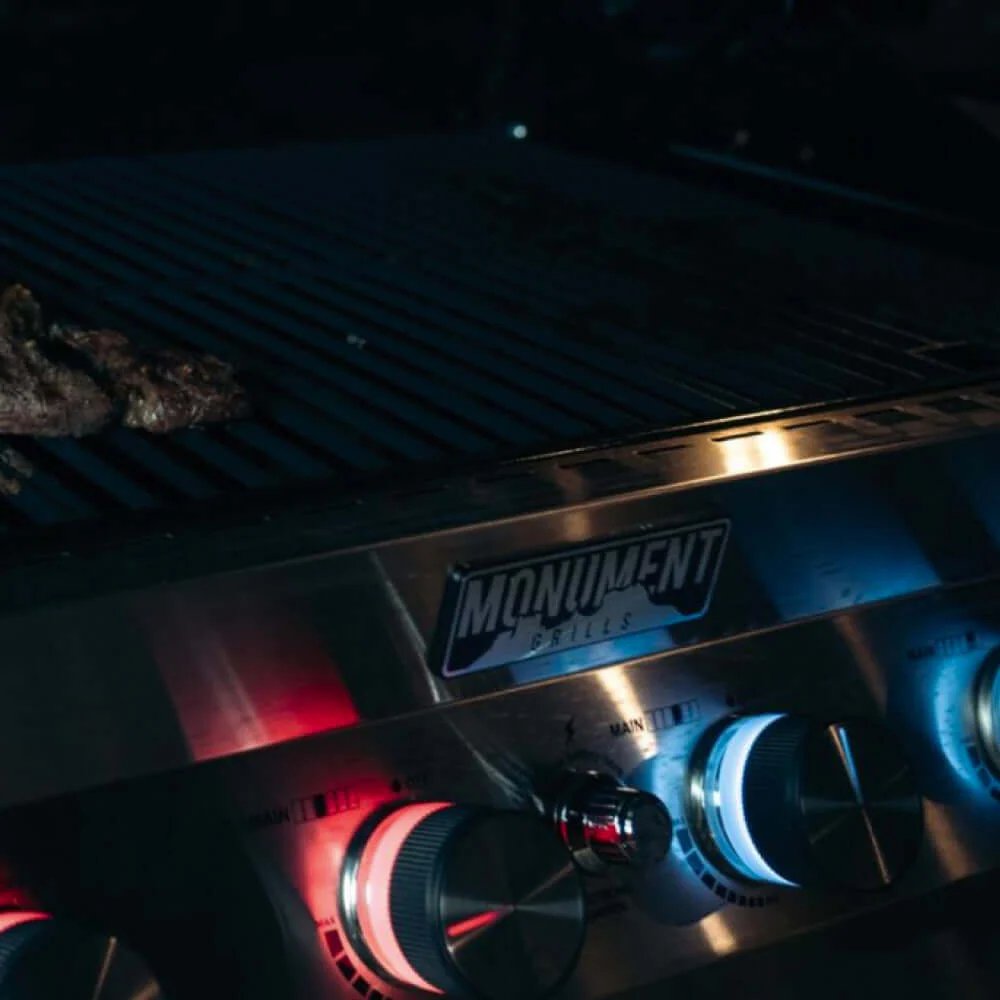 Close-up of a Monument Grills Denali 605 with glowing red burners in a dark setting