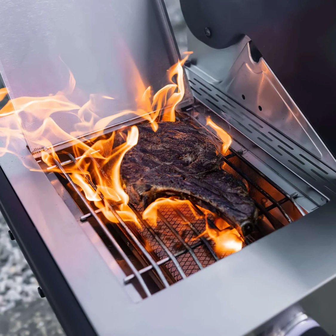 Flaming grill with a steak cooking inside Monument Grills Denali 605 Pro