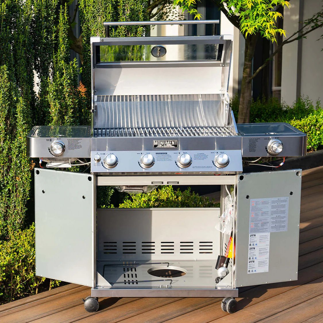 Stainless steel grill on a wooden deck with greenery in the background