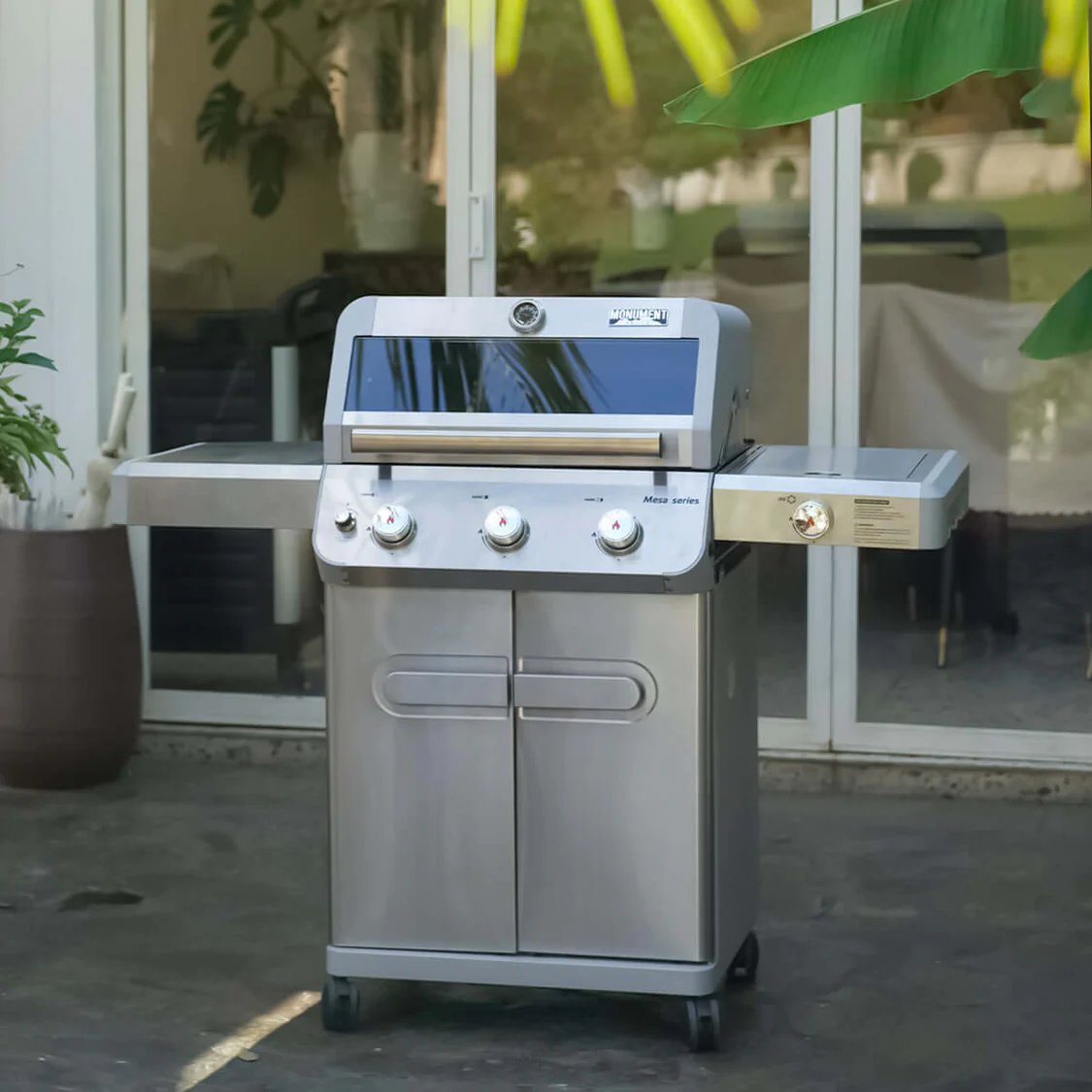 Stainless steel outdoor Monument Grills Mesa 305 on a patio with plants and furniture in the background