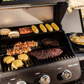 Monument Grills Mesa 325 propane gas grill with ribs, vegetables, and bread cooking on the grates.