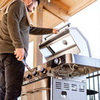 Man adjusting a stainless steel outdoor grill in an outdoor setting