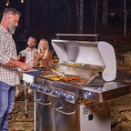 People grilling outdoors at night with a large stainless steel grill.