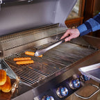Person grilling hot dogs on a stainless steel barbecue grill.