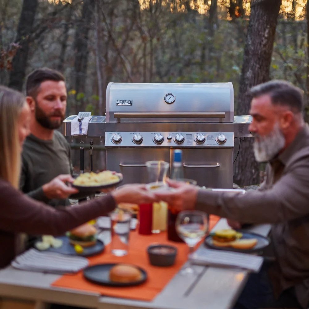Group of people enjoying a meal around a grill outdoors.