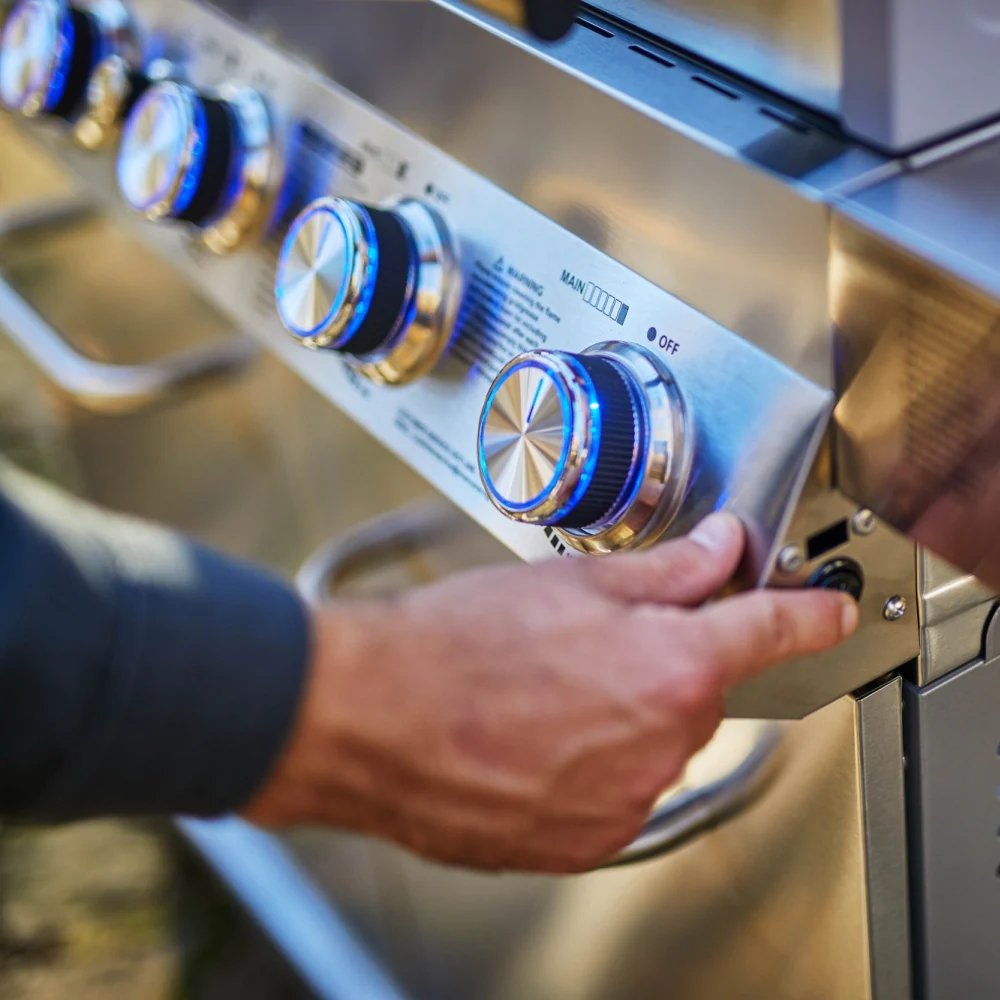 Hand adjusting knobs on a stainless steel outdoor grill with blue lights.