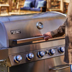 Stainless steel grill with a person opening the lid outdoors