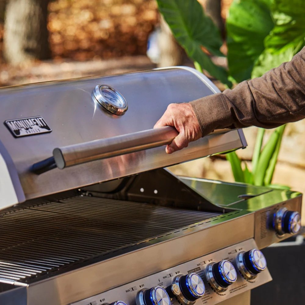 Person opening a stainless steel grill with a blurred natural background