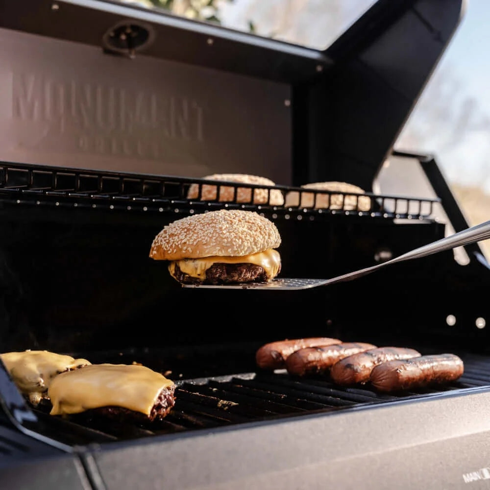 Grilling burgers and hot dogs on a portable grill with 'Monolith' branding.