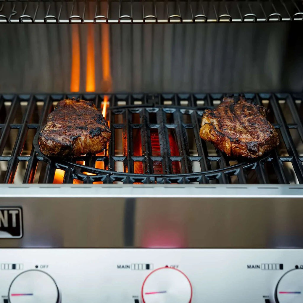 Two steaks cooking on a grill with visible flames and control knobs.
