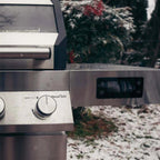 Stainless steel grill with control knobs in a snowy outdoor setting
