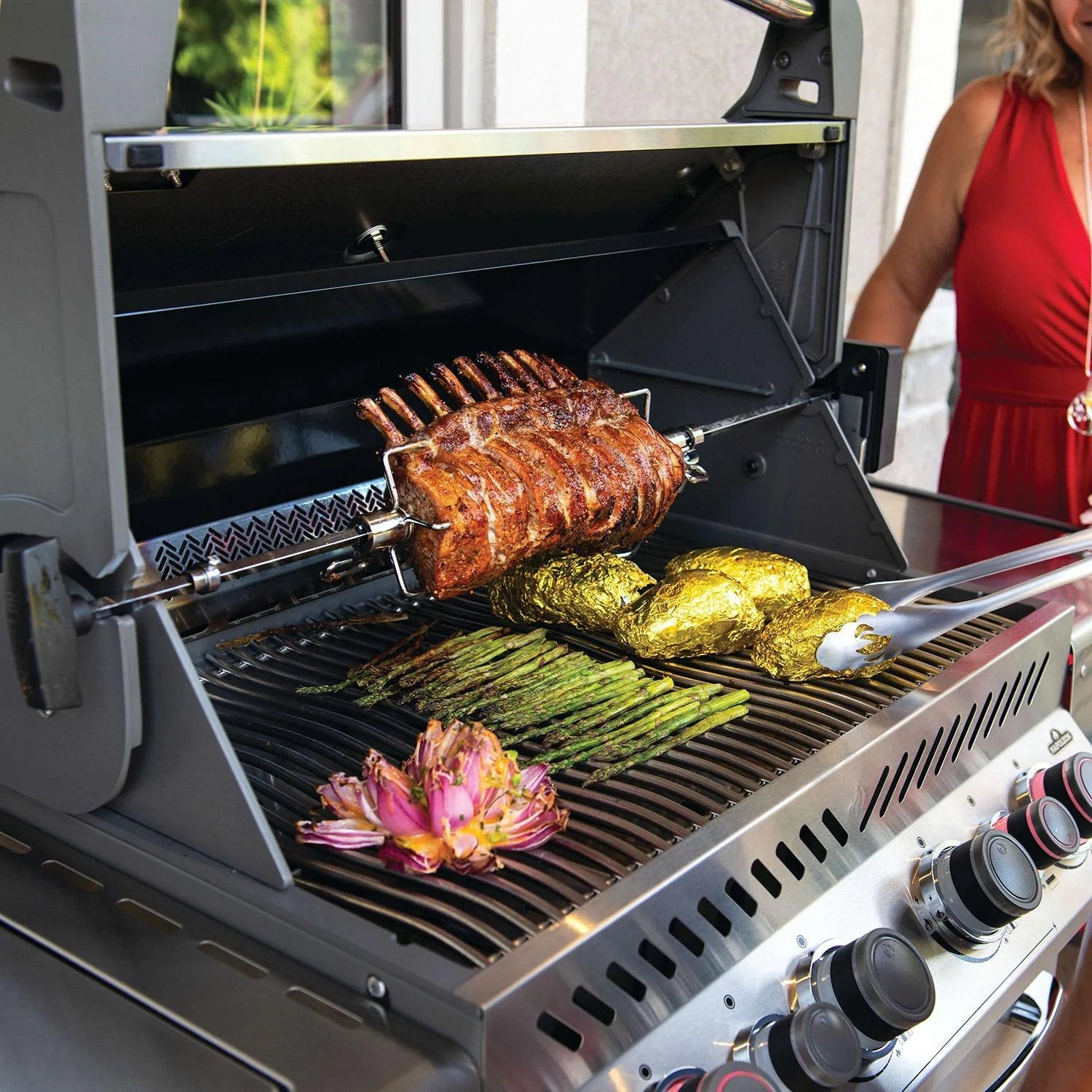 Grilled rack of ribs with asparagus, foil-wrapped potatoes, and artichoke on a BBQ grill